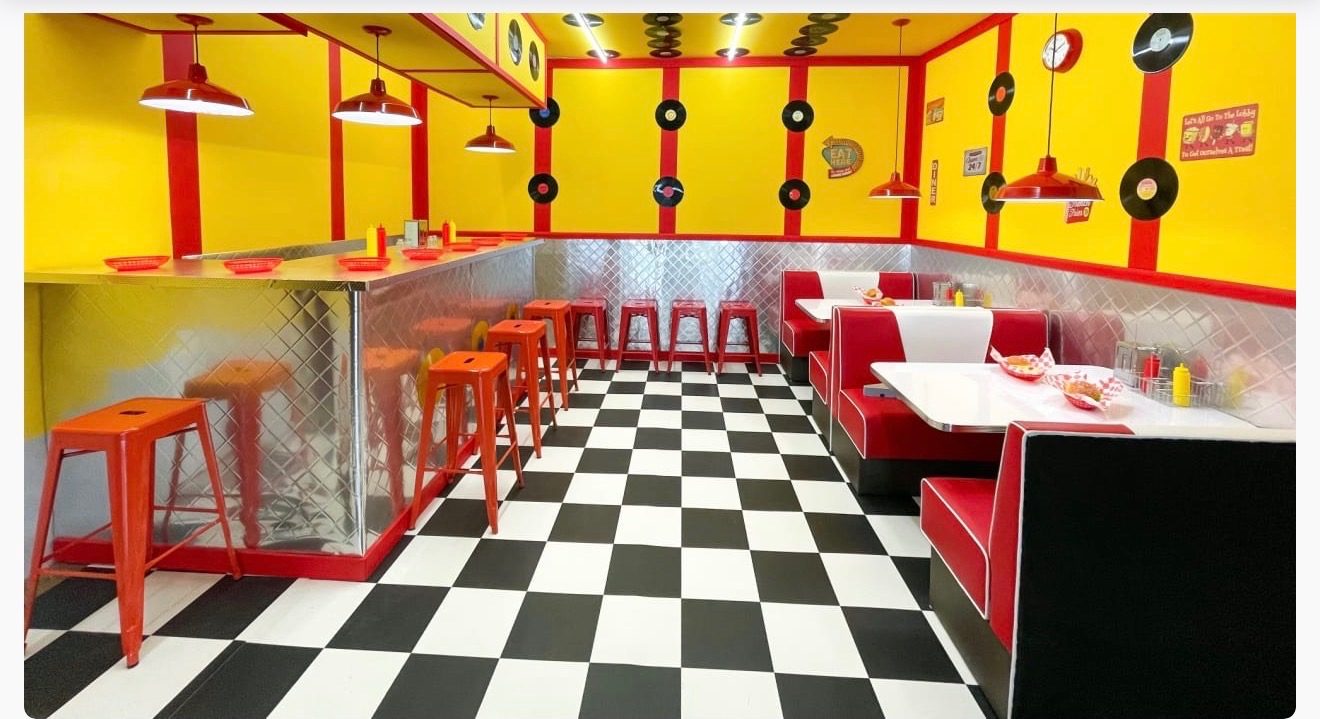 Retro diner set with a black-and-white checkered floor, red booths, and vinyl records on the walls