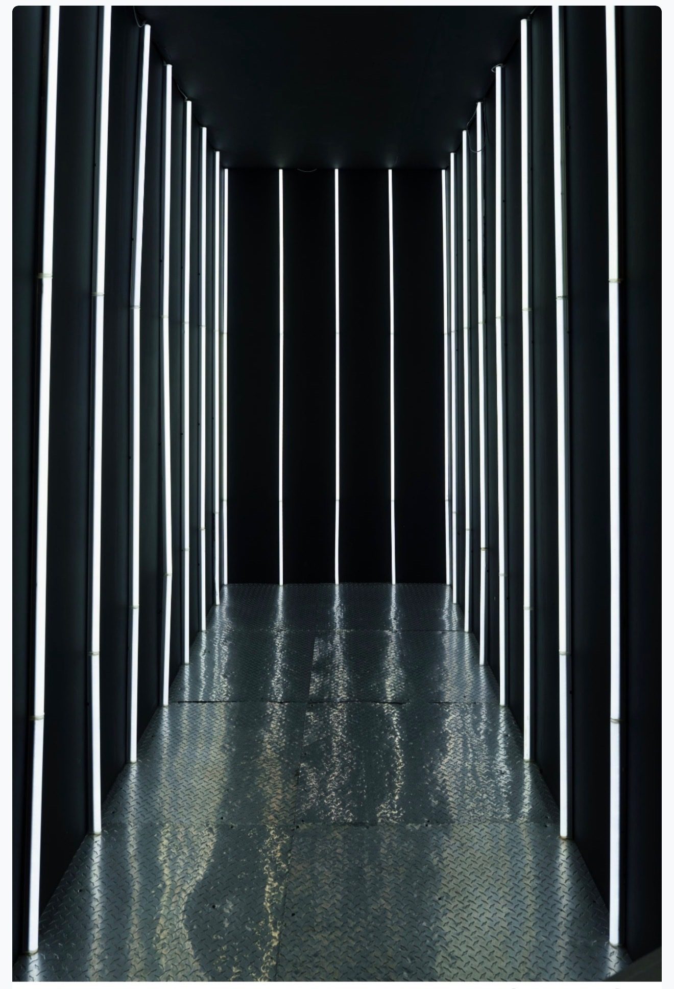 Black neon-strip tunnel set lined with vertical white LED tubes and a diamond-plate floor