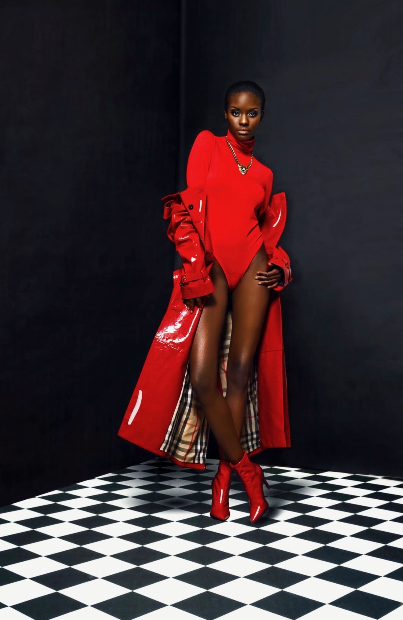 Model in a red bodysuit and red patent trench coat on a checkered floor